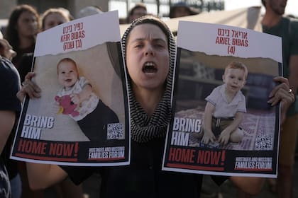 Una mujer sostiene carteles de Kfir y Ariel Bibas, cautivos de Hamas junto con sus padres en la Gaza, durante una marcha hacia el Parlamento de Israel para pedir un acuerdo para liberar a los rehenes, en Jerusalén, el jueves 13 de junio de 2024