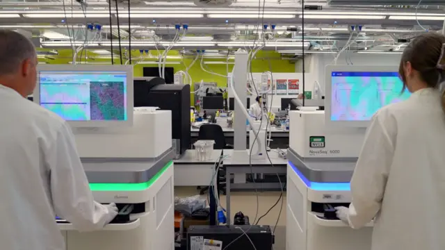 Dos científicos de espaldas a dos secuenciadoras blancas de alta tecnología. Dos científicos de espaldas a dos secuenciadoras blancas de alta tecnología.